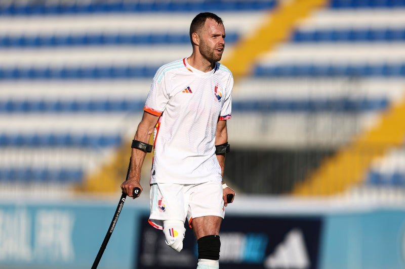 Joueur belge en blanc attend le ballon, appuyé sur ses béquilles